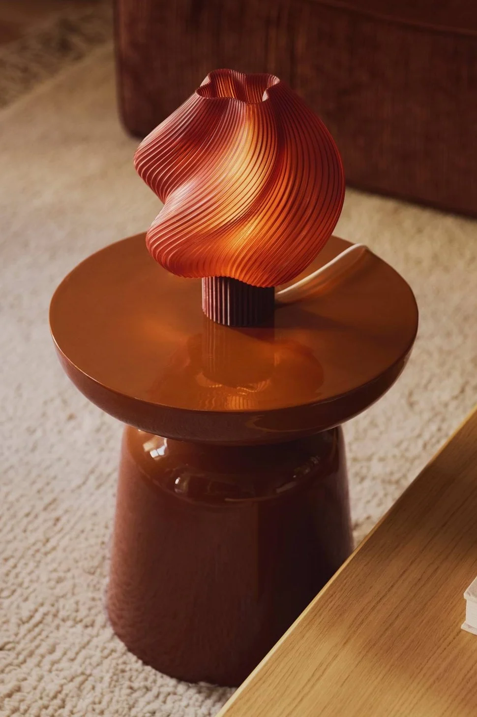 A warmly lit, wavy orange pleated lamp sits on a glossy brown side table.