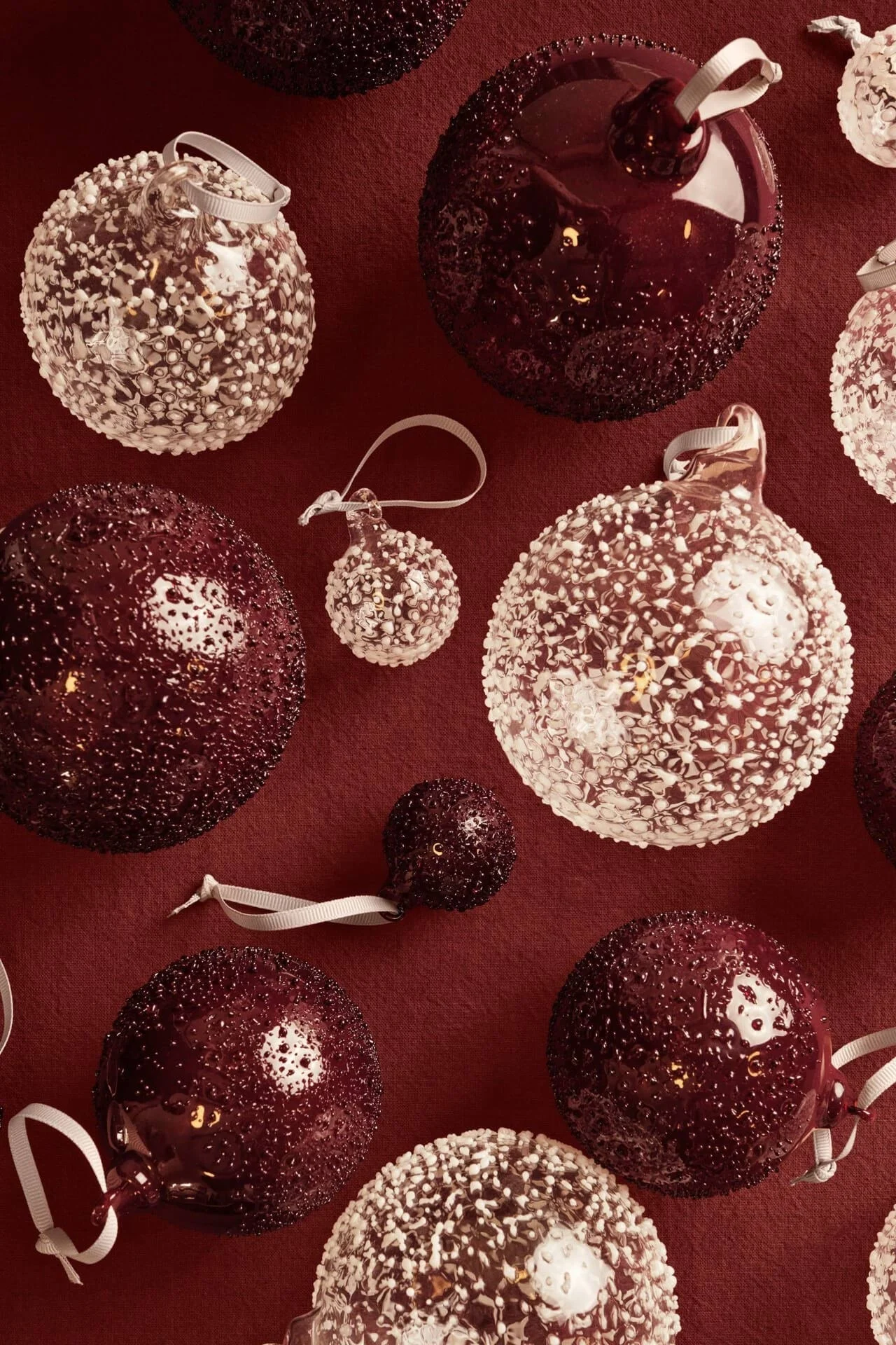 Clear and maroon textured Christmas ornaments of various sizes scattered on a deep red background.