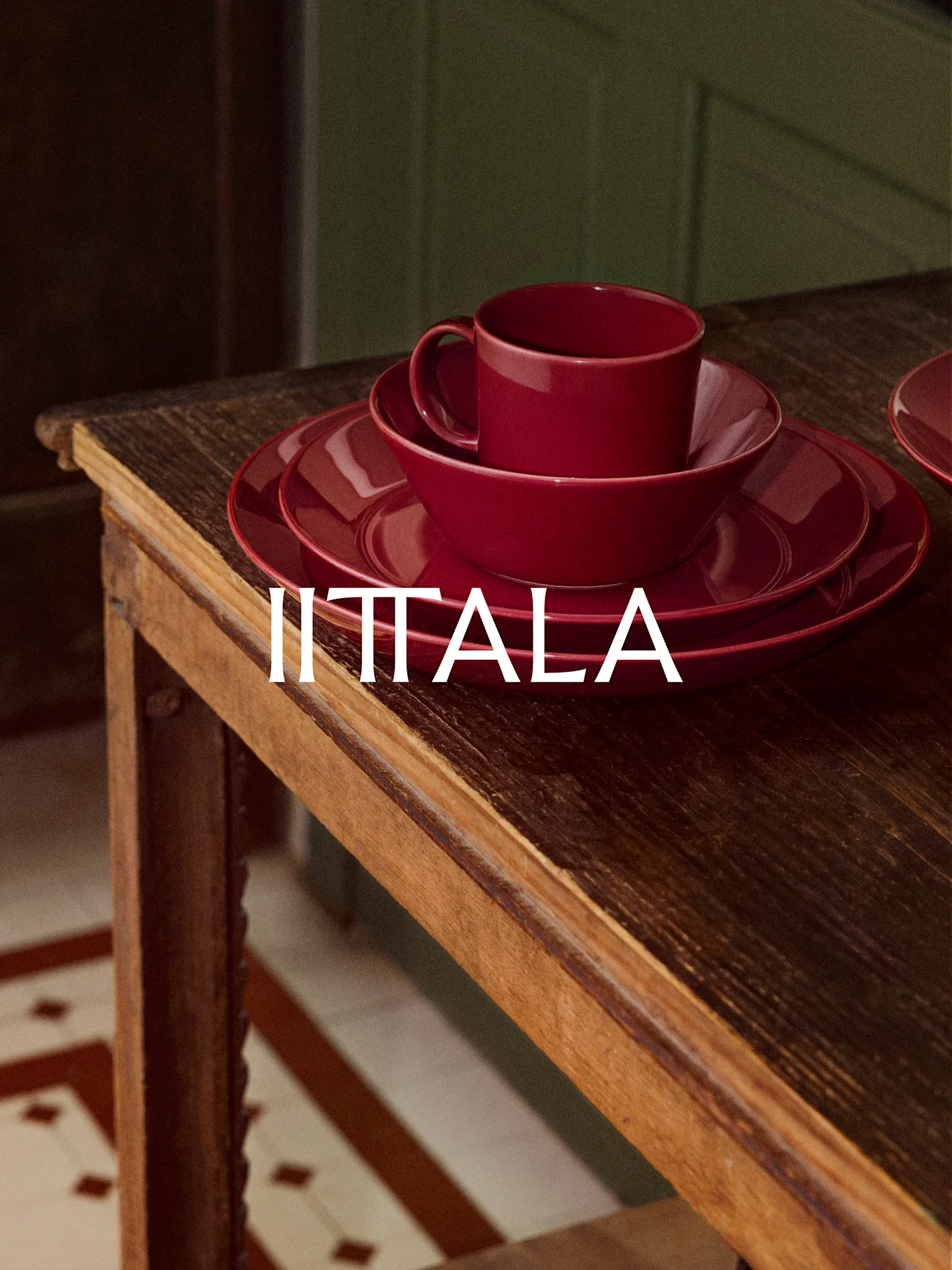 A stack of red IITTALA dinnerware, including a cup, bowl, and plates, sits on a rustic wooden table.