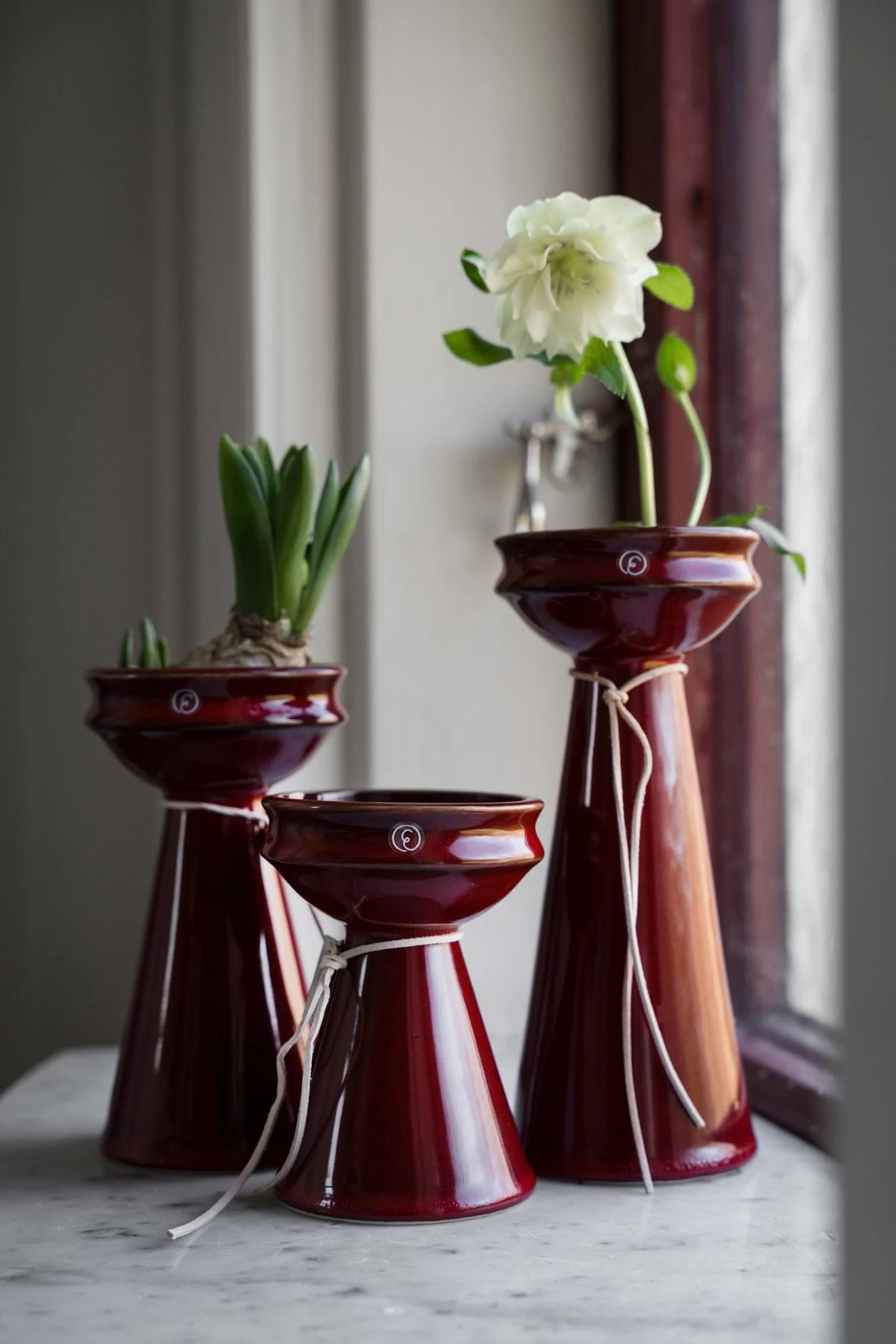 Three dark red ceramic vessels with a wide top and conical base, two holding plants, tied with white string.