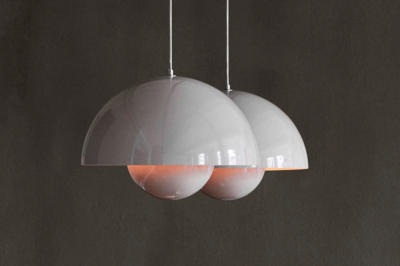 Two glossy grey pendant lamps with an orangey glow from below hang against a dark background.
