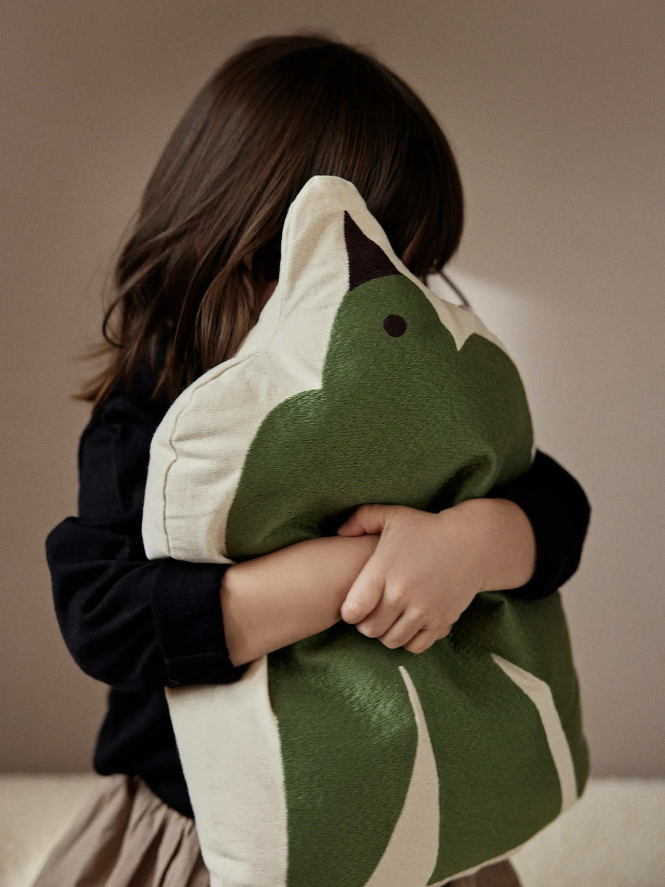 Child from behind hugging a green and beige leaf-shaped pillow.