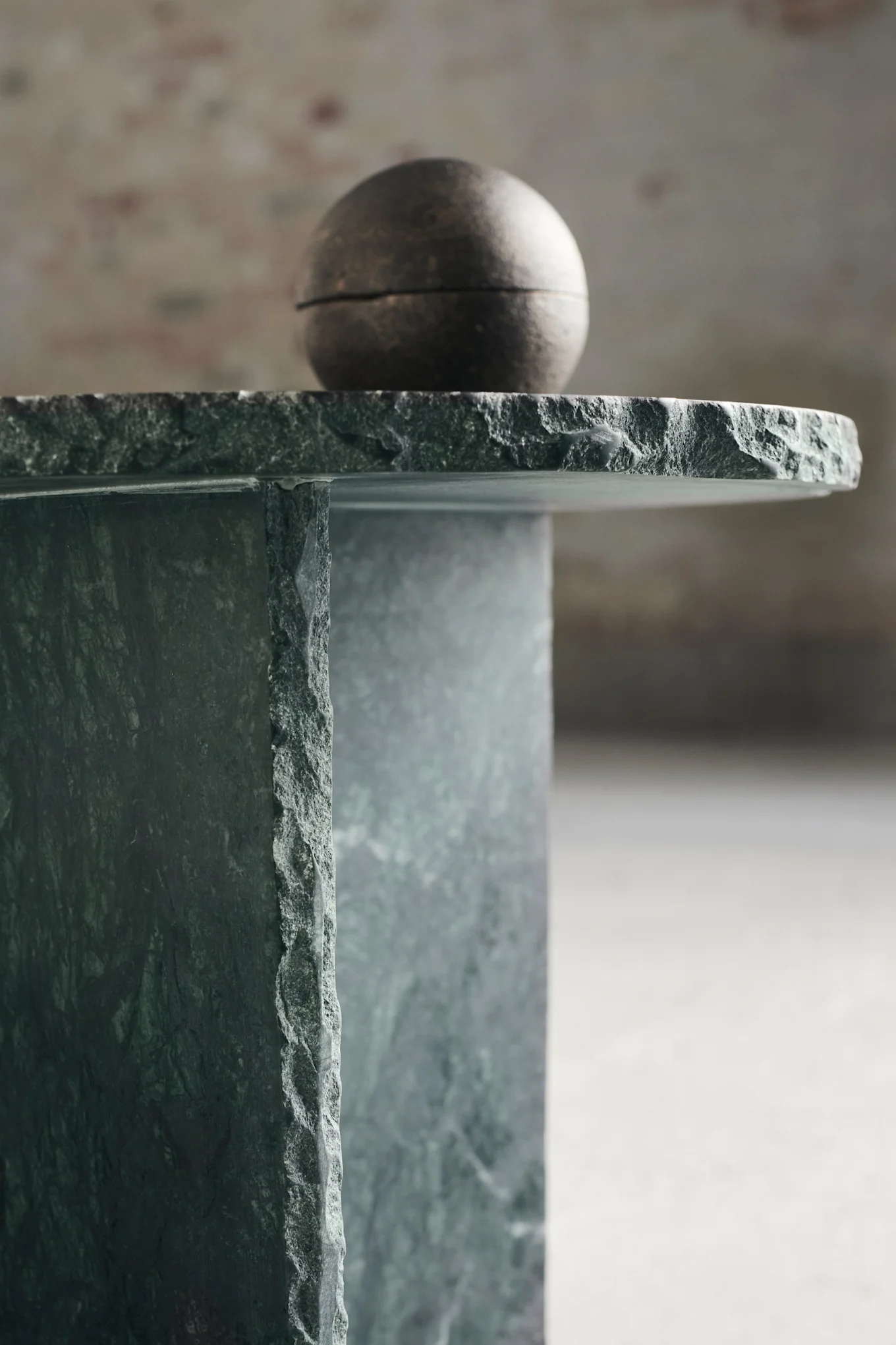 Dark green marble side table with rough edges and a spherical metallic object on top.