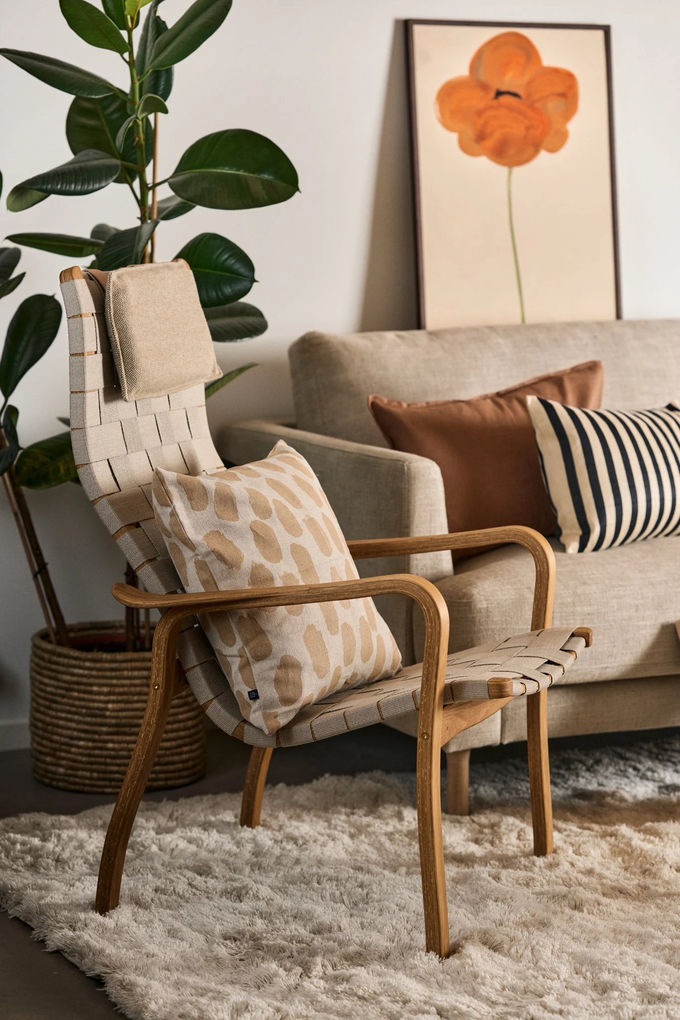 Light-colored woven lounge chair with a patterned cushion in a living room setting, featuring a sofa and plant.