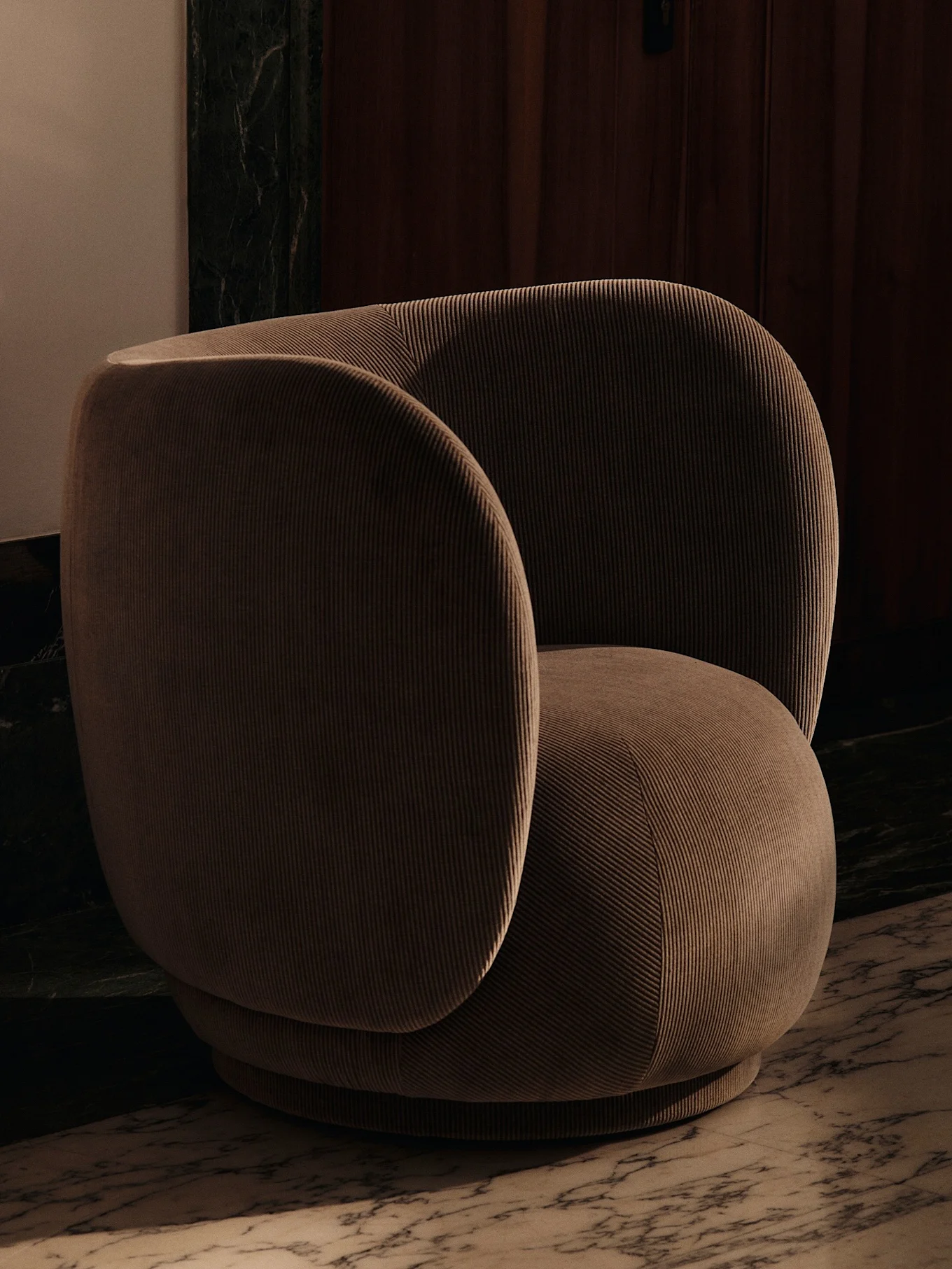 A modern, rounded armchair upholstered in ribbed brown corduroy fabric, set on a marble floor.