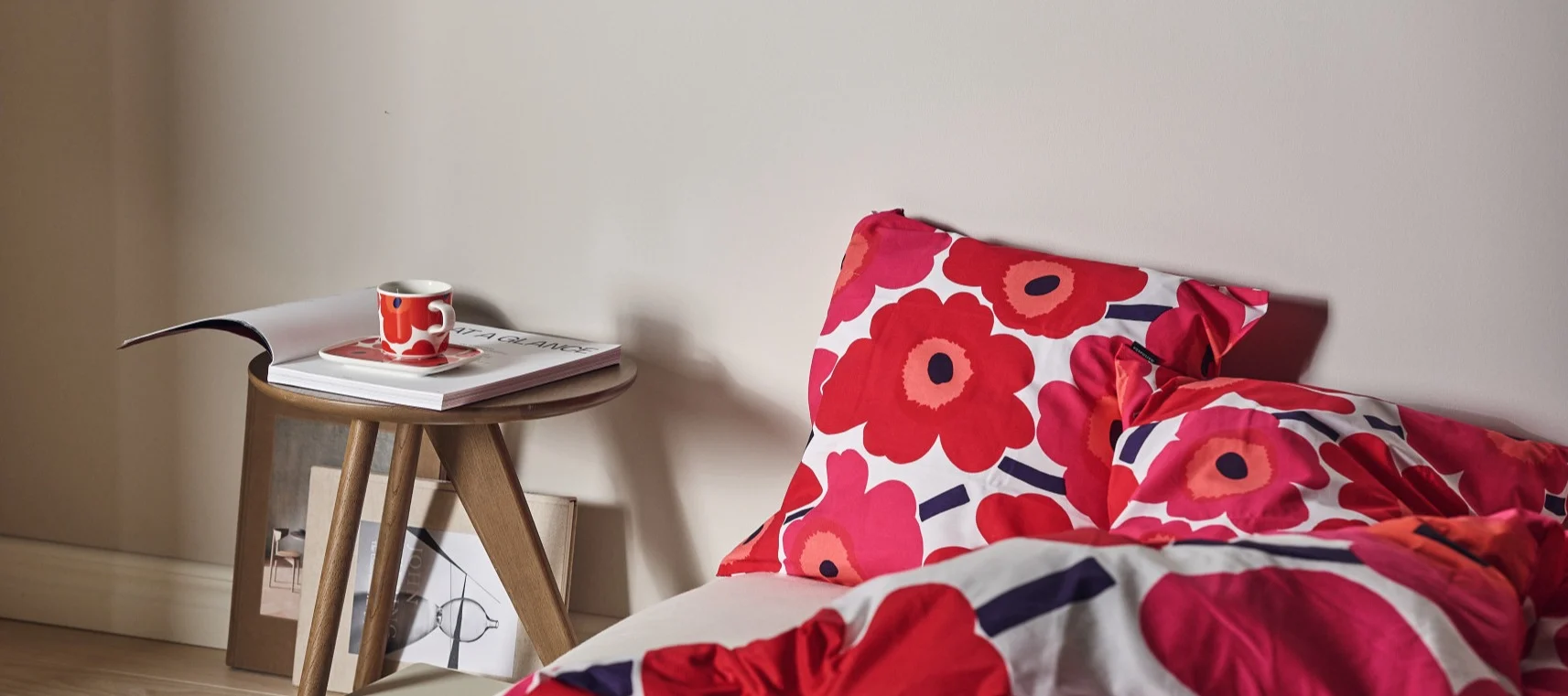 Bed with red floral bedding, a matching cup on a side table with a magazine.