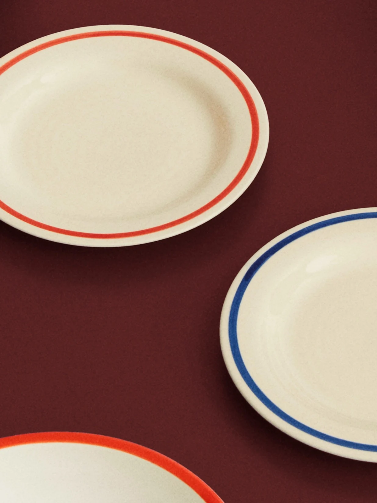 Three cream oval plates with red and blue rims on a dark red surface.