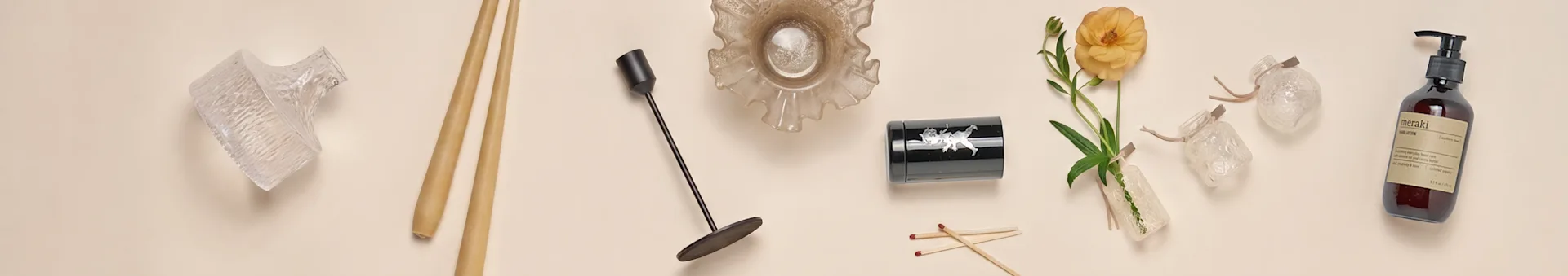 A collection of home decor items, including glass vases, chopsticks, a black candlestick, a ruffled glass bowl, a black container, an orange flower, and a hand lotion bottle.