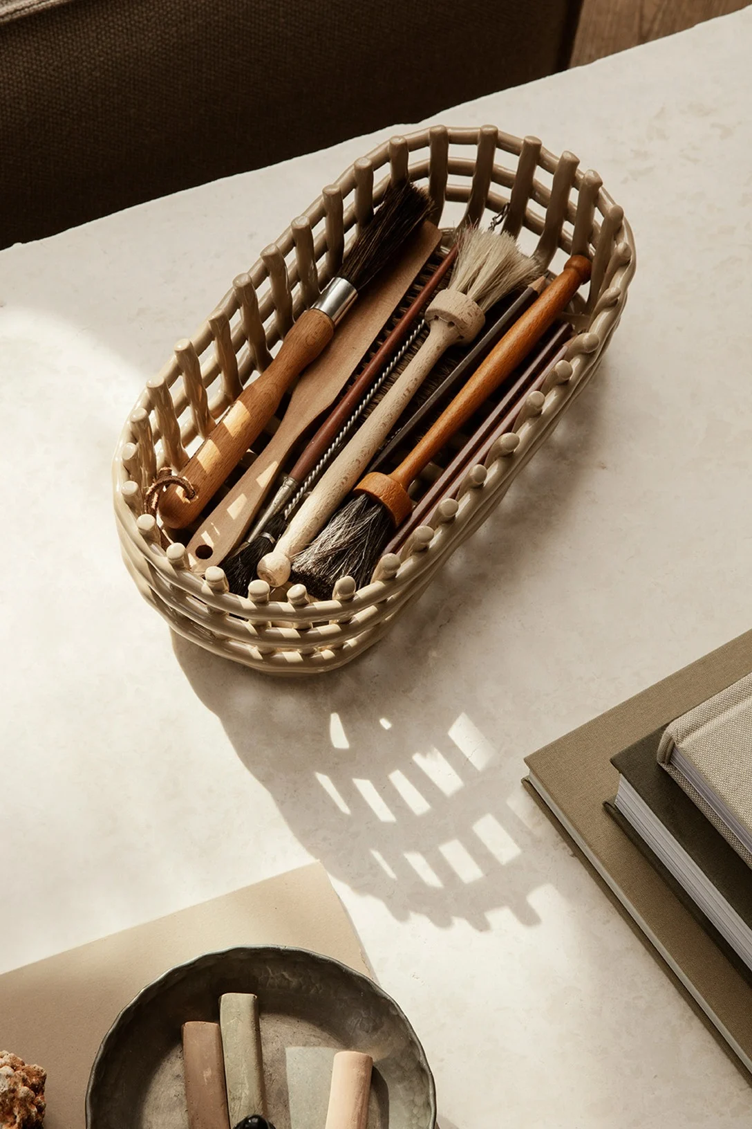 The Ferm Living ceramic basket helps you declutter your home, seen here filled with paint brushes and placed on a desk. 