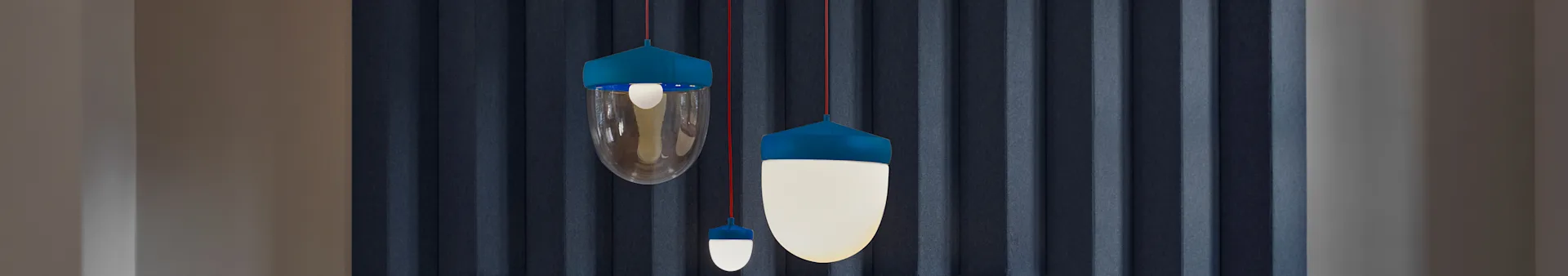 Three modern pendant lights with teal tops and red cords, featuring clear and opaque white globe-shaped shades, against a dark blue textured wall.