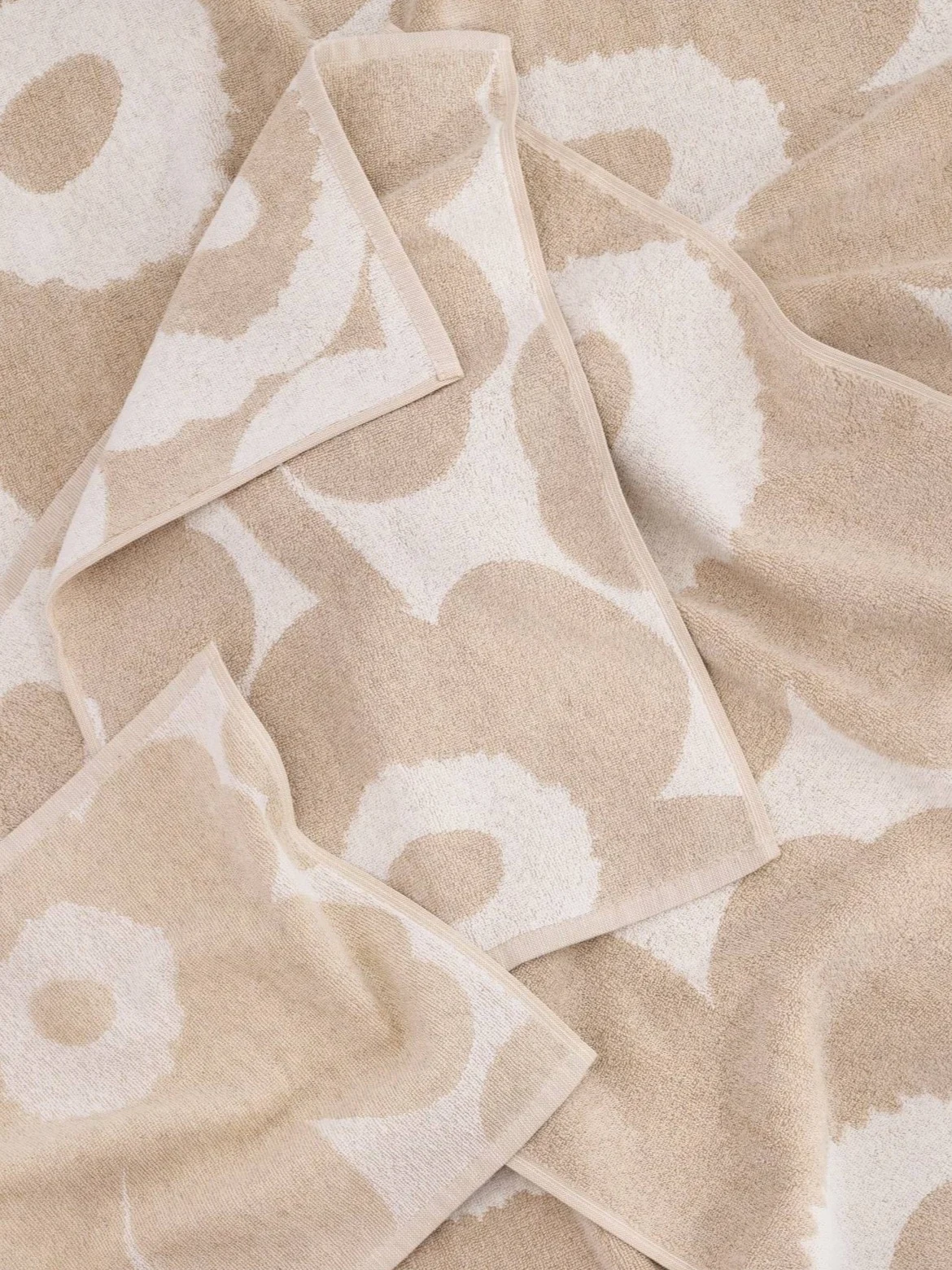 Several folded beige and off-white towels with a large floral pattern.