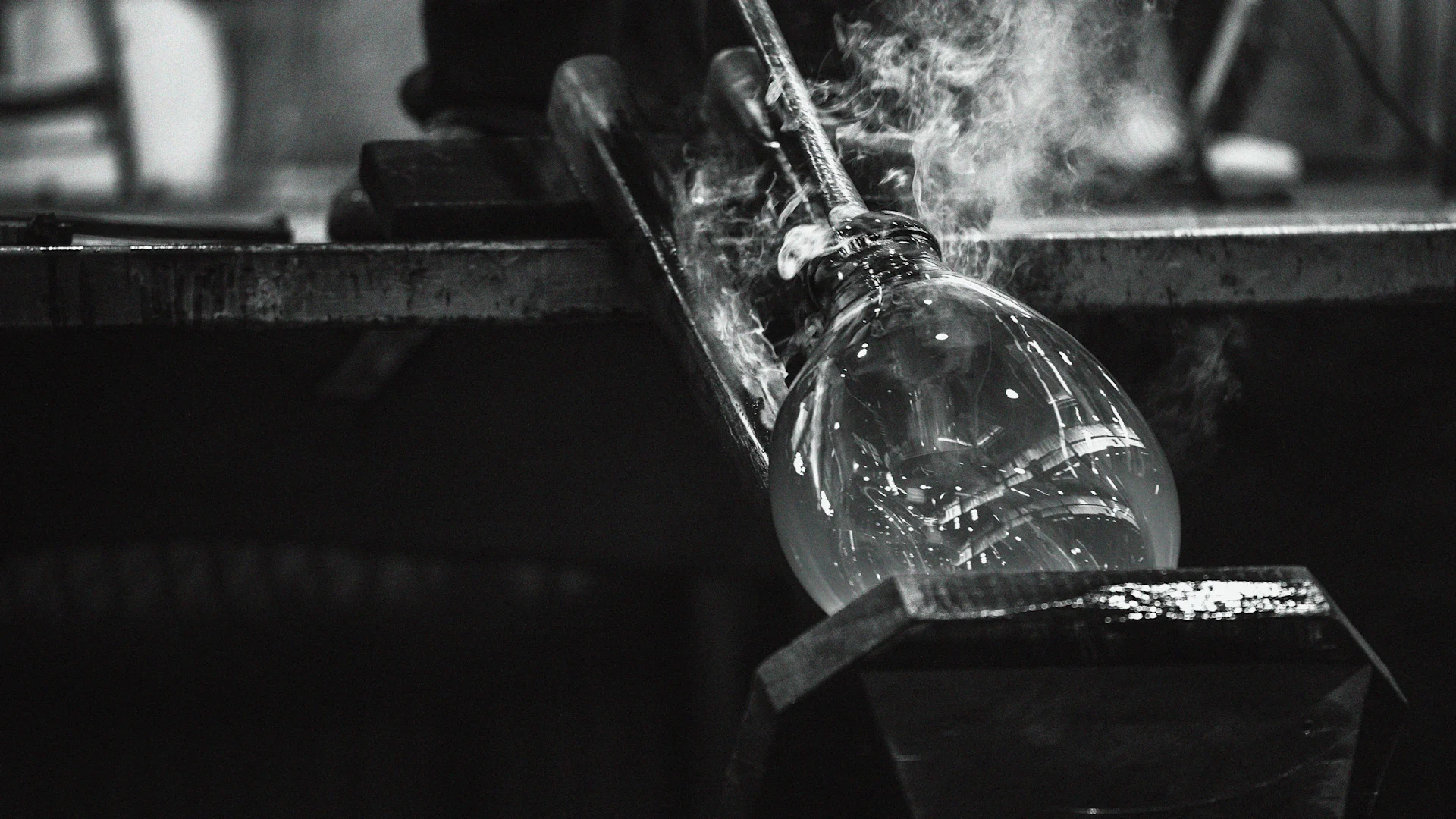 Black and white: A clear glass vessel being shaped by a glassblower, with steam rising from the hot material.