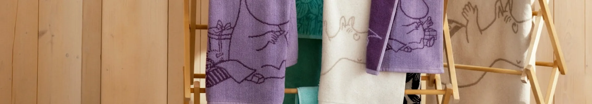 Purple, green, white, and beige towels with various embroidered patterns hanging on a wooden ladder rack.