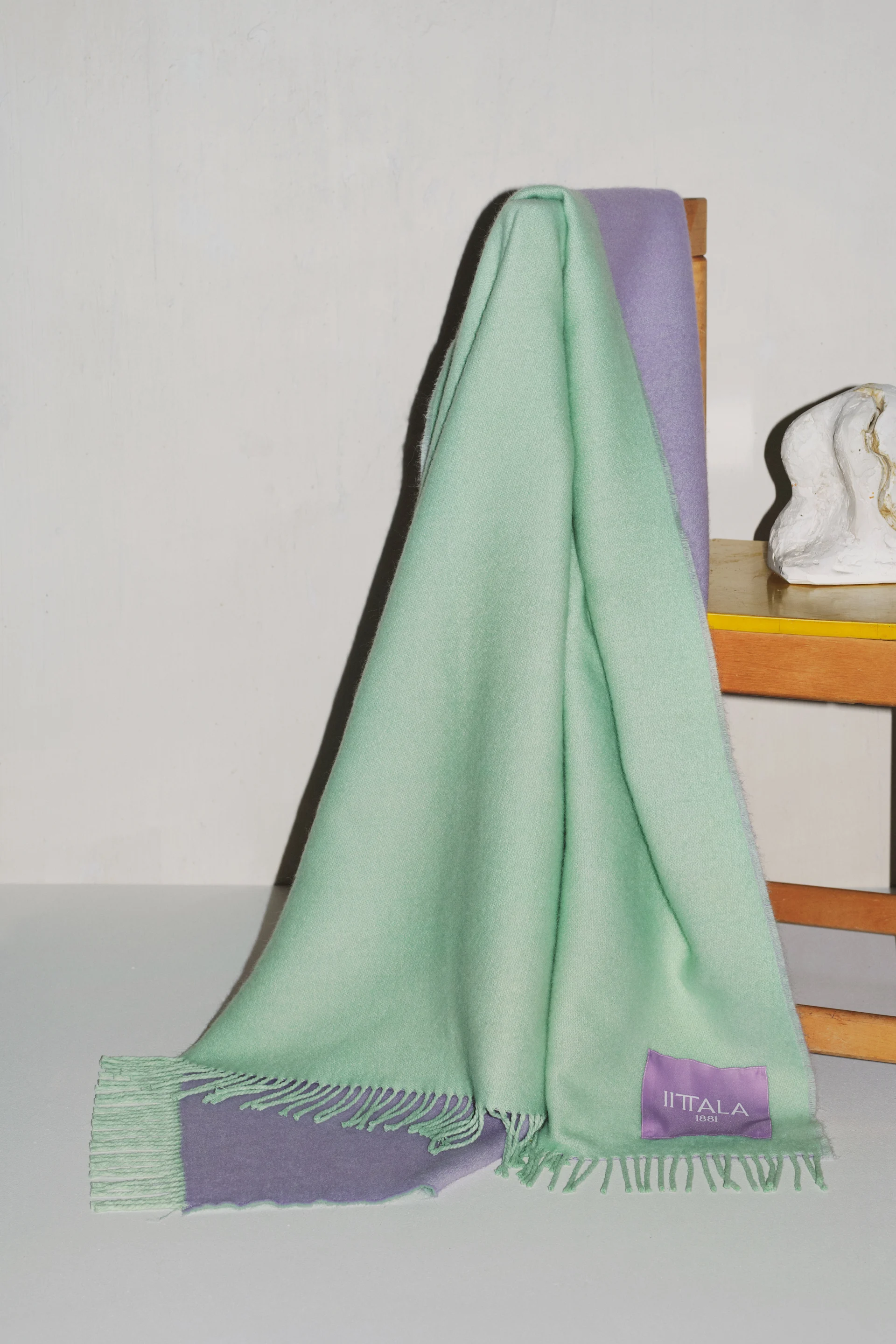Mint green and lavender two-toned blanket with fringe draped over a wooden chair.