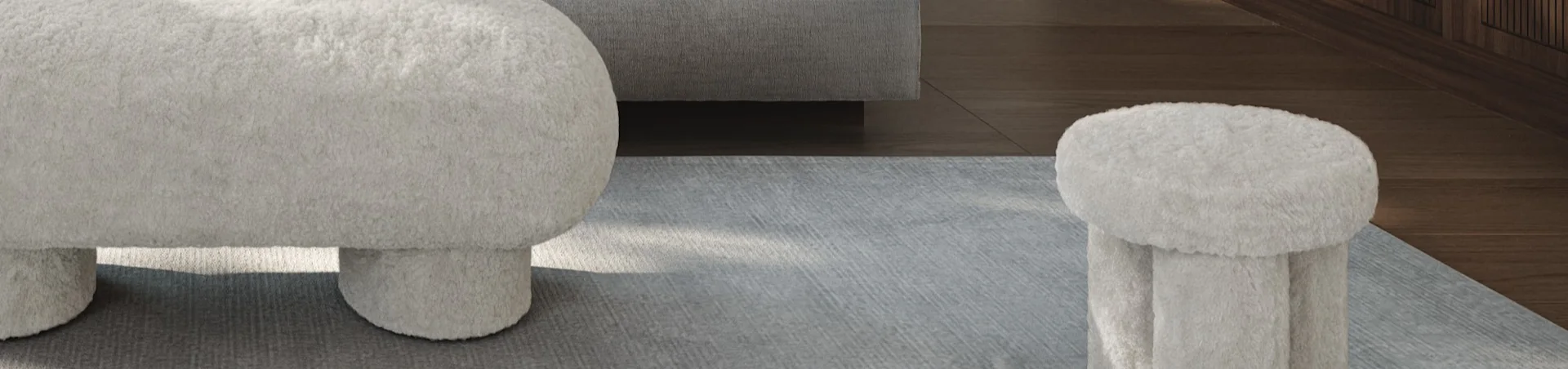 Two fluffy off-white ottomans on a grey rug, with a grey sofa and wooden floor in the background.