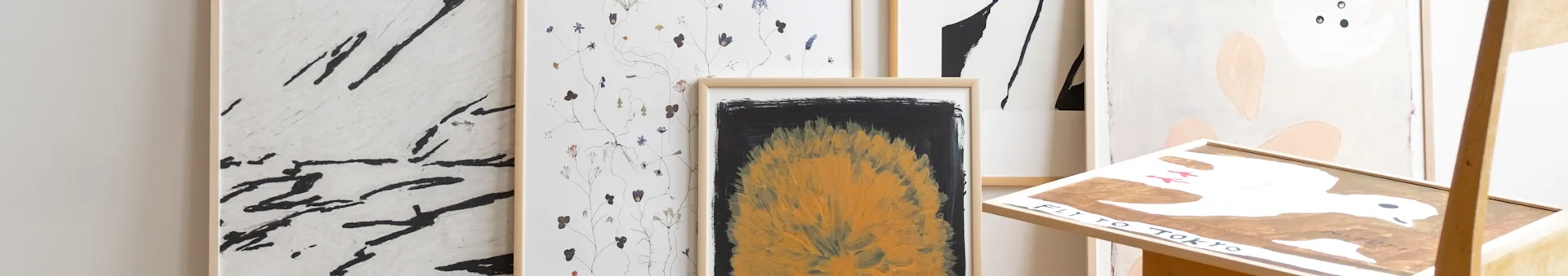 A collection of framed artworks: abstract black strokes, pressed flowers, a yellow flame-like painting, and a piece titled 'FLY TO TOKYO'.