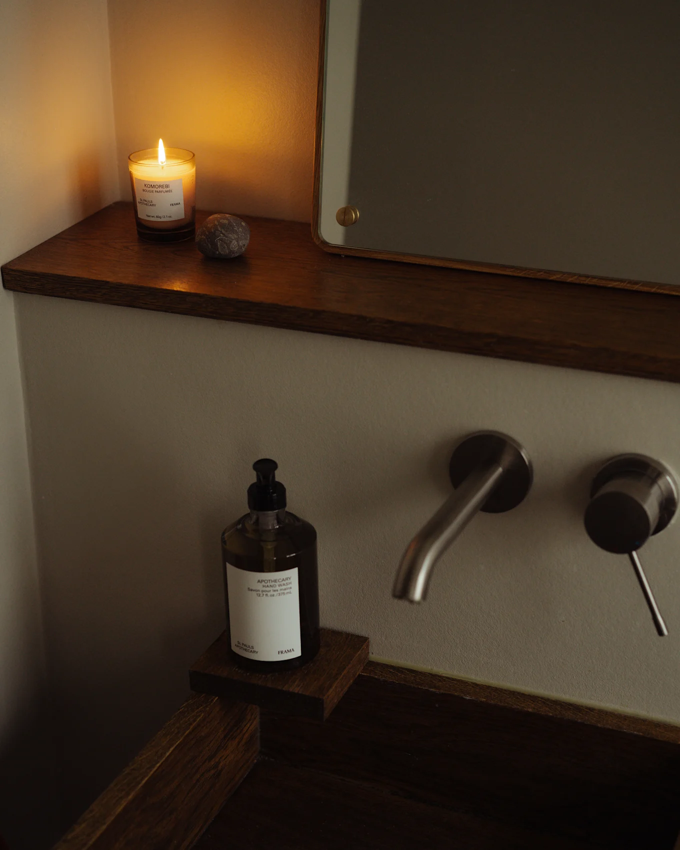 Cozy bathroom with a lit candle, hand wash bottle, and brushed metal faucet on a dark wood sink.